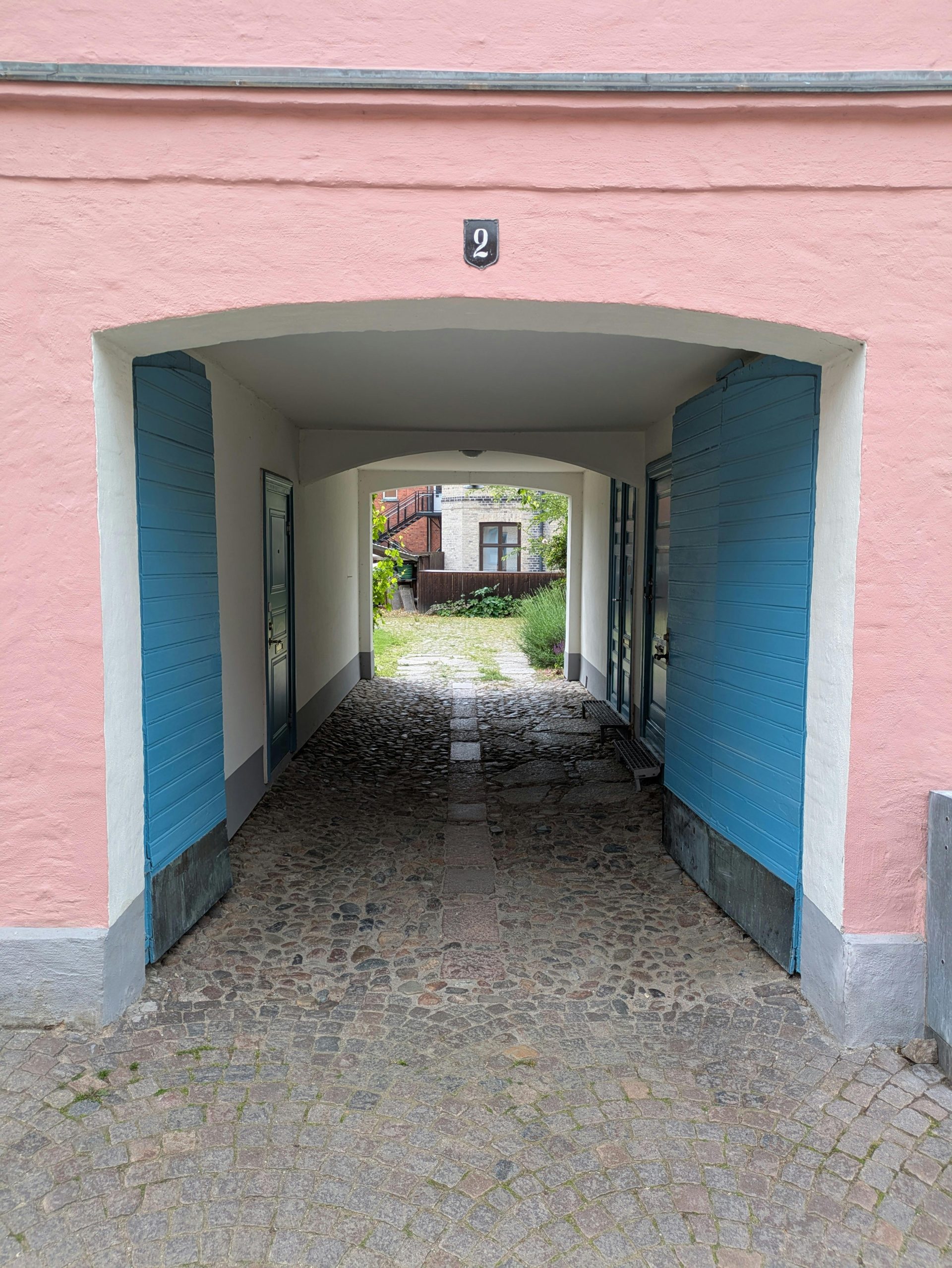 A quaint archway leading to a cobblestone courtyard with pastel colors and rustic charm.
